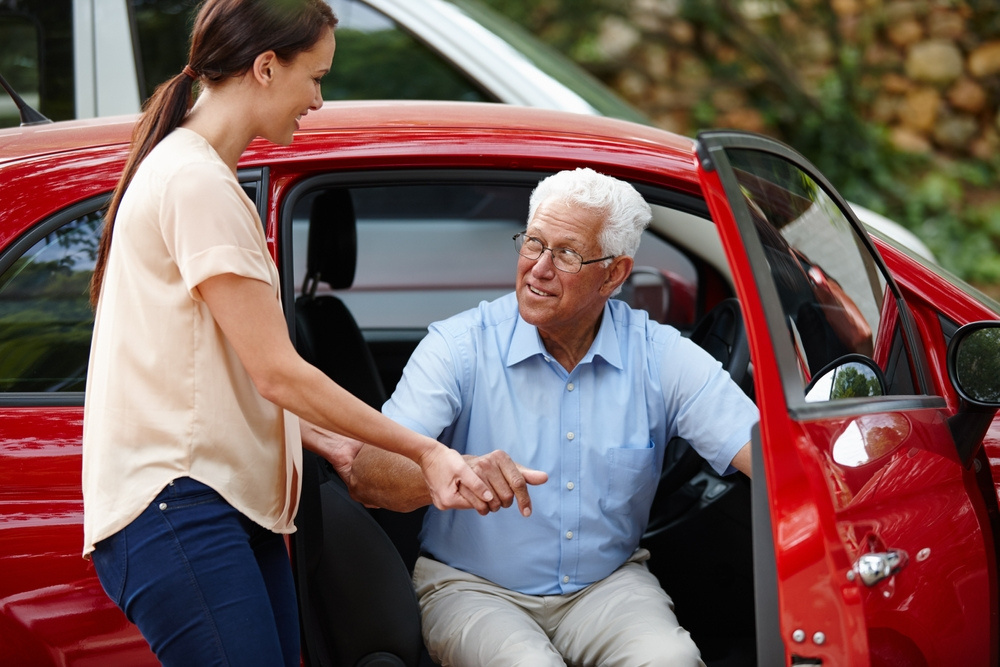 A companion helping an older gentleman out of the car for an outing